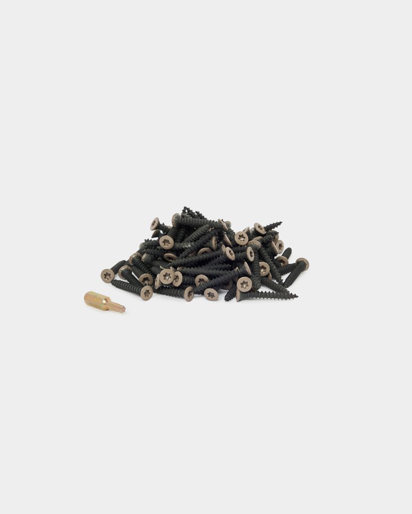 WoodUpp pile of black coated wood screws with coarse threads and countersunk Torx heads, arranged in a small heap on a white background, accompanied by a single gold-colored screwdriver bit. The image highlights WoodUpp screws and the matching driver bit for decking or timber assembly.