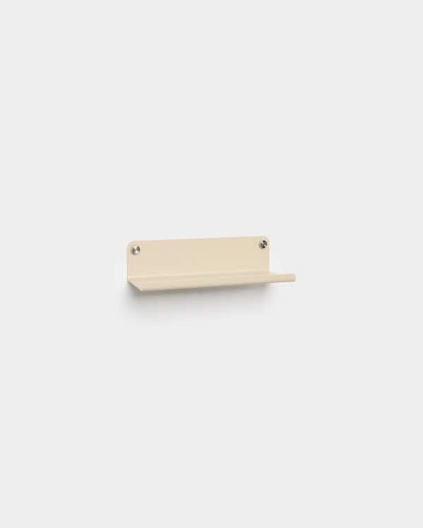 WoodUpp wall-mounted metal mini shelf in matte beige, shown fixed to a white wall with two visible round stainless fasteners. The minimalist single-tier shelf features a small raised lip and rounded corners, suitable for holding a phone, keys, or small decorative items.
